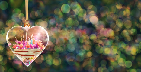 Poczt&oacute;wka urodzinowa - przezroczysta bombka  w kształcie serca z tortem urodzinowym w środku na tle kolorowych rozmyć świateł bokeh