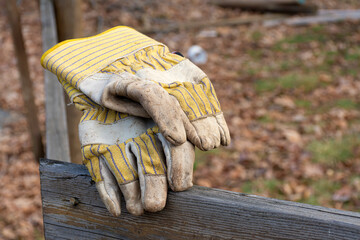 Old worn out and faded yellow work gloves resting on a wooden fence. 