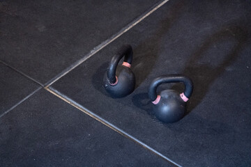 In a gym, two kettlebells can be seen sitting on the tiled floor