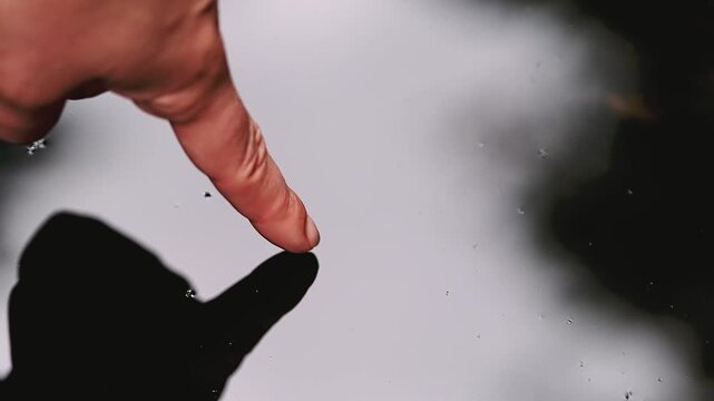 Human finger touching water surface creating concentric ripples