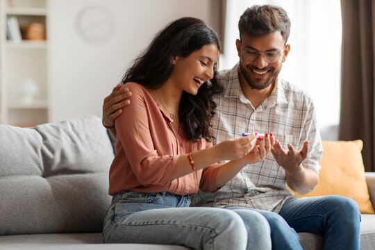 We'll be parents. Excited Indian couple holding positive pregnancy test, sitting on sofa at home. Family moments, childbirth concept - Powered by Adobe