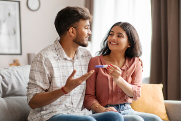 New life, childbirth. Happy Indian spouses holding positive pregnancy test cuddling on sofa at home, awaiting to be parents