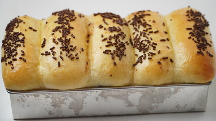 Torn bread filled with chocolate topped with chocolate sprinkles and golden brown in color which is freshly cooked and still in an aluminum baking pan and placed in a white place (isolated white).