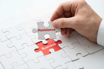 Hand placing white jigsaw puzzle piece labeled Assistance above red Business gap in puzzle