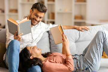 Indian man and woman reading books while resting on comfy sofa, spouses enjoying leisure time at home on weekend