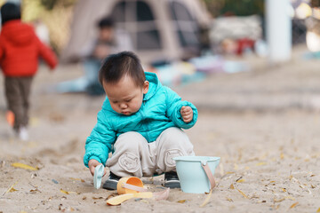 An Asian boy playing in a sandbox at a playground in winter