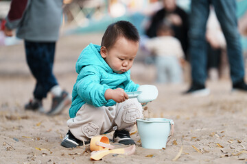 An Asian boy playing in a sandbox at a playground in winter