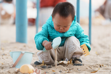 An Asian boy playing in a sandbox at a playground in winter
