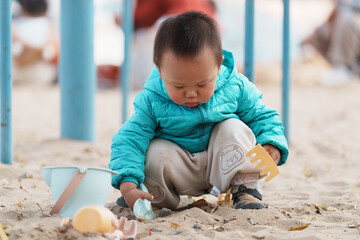 An Asian boy playing in a sandbox at a playground in winter