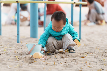 An Asian boy playing in a sandbox at a playground in winter