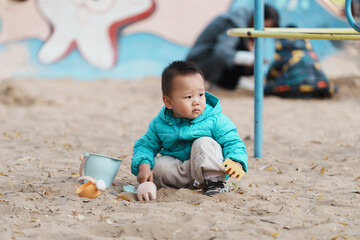 An Asian boy playing in a sandbox at a playground in winter