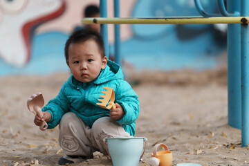 An Asian boy playing in a sandbox at a playground in winter