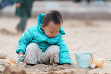An Asian boy playing in a sandbox at a playground in winter