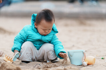 An Asian boy playing in a sandbox at a playground in winter