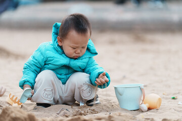 An Asian boy playing in a sandbox at a playground in winter