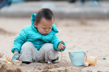 An Asian boy playing in a sandbox at a playground in winter