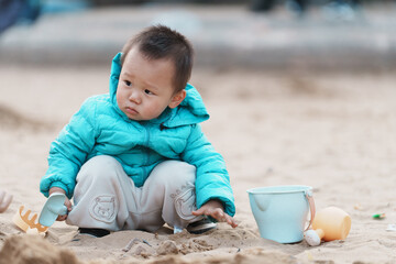 An Asian boy playing in a sandbox at a playground in winter
