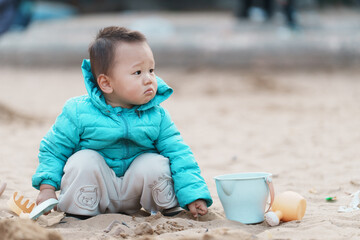 An Asian boy playing in a sandbox at a playground in winter