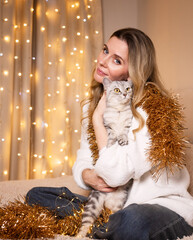 A young woman with Christmas decorations and her beloved cat at home preparing for Christmas