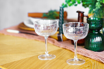 Close up of elegant crystal glasses, plates and flowers on wooden table with green decorations and warm holiday ambiance. Perfect for celebrations, cozy and romantic gatherings, seasonal home decor.