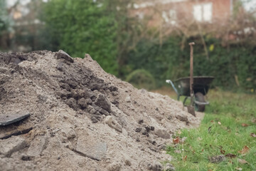 Construction work in the yard of a private home, a wheelbarrow a shovel and a pile of earth against the backdrop of a modern building 
