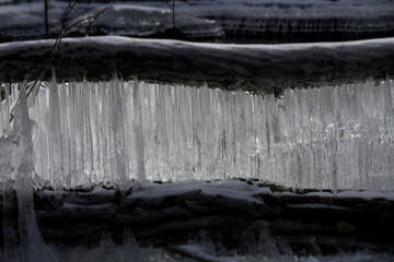 Icicles are forming along the edge of a log, creating a natural curtain of ice. The contrast between the dark wood and bright ice is striking.