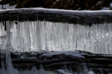Icicles are forming along the edge of a log, creating a natural curtain of ice. The contrast between the dark wood and bright ice is striking.