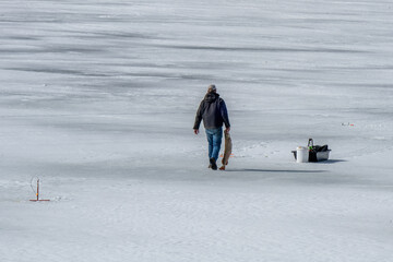 A person walks across a snow-covered frozen lake, carrying a large fish in one hand. 