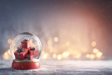 Fototapeta premium Boule à neige remplie de cadeaux rouges sur neige avec forêt floue et lumières dorées en arrière-plan, décor féerique avec espace négatif copyspace pour noël et fêtes de fin d’année