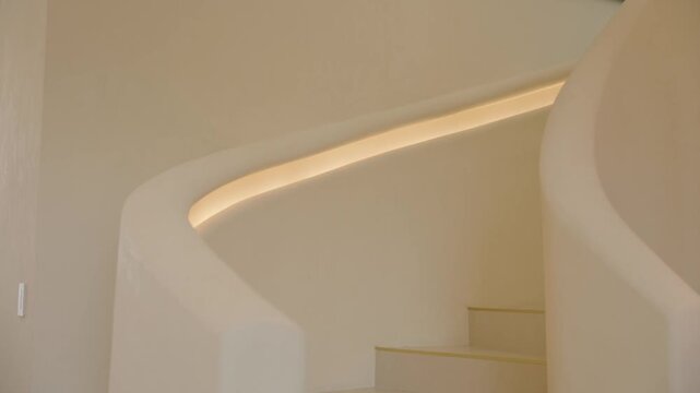 Curved white staircase with built in handrail glows warmly. Smooth walls and clean lines create quiet, modern space with soft light and elegant architectural flow.