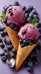 Scoops of creamy blueberry ice cream in waffle cones garnished with fresh blueberries and mint leaves
