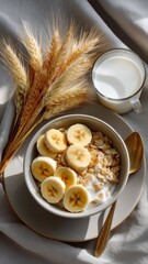 A bowl of cereal topped with banana slices and served with a glass of milk, alongside dried wheat decorations