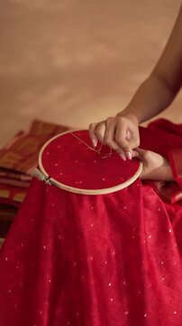 Close up of hands working on embroidering a red saree in 4K, showing detailed craftsmanship, intricate threadwork, and traditional Indian textile artistry.