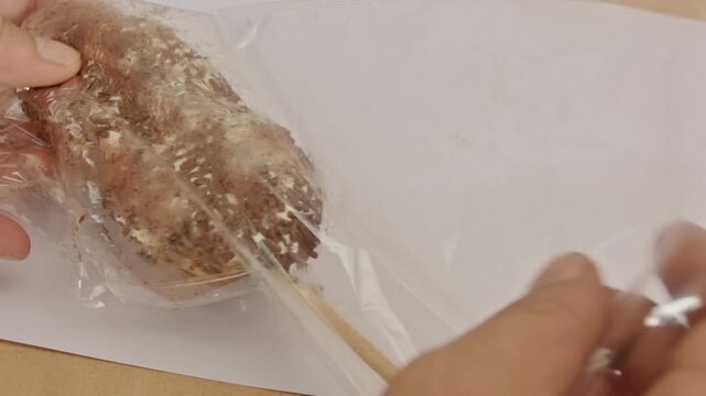 Hand opening transparent plastic packaging of chocolate sprinkles sweet bread on a skewer