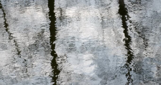 Abstract of distorted reflections of bare trees and a light sky on a gently rippled water surface in spring, Mustavuori, Helsinki, Finland.