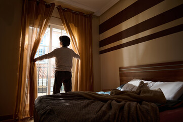 Person Opening Curtains in Sunlit Bedroom by Balcony Door With Striped Wall