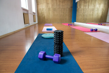 Unrolled pilates and yoga mat on wooden floor in fitness studio. Modern gym interior with equipment, daylight. Healthy lifestyle concept. Sports fitness equipment, women's, yoga blocks, dumbbells