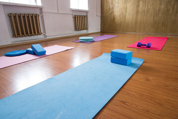 Unrolled pilates and yoga mat on wooden floor in fitness studio. Modern gym interior with equipment, daylight. Healthy lifestyle concept. Sports fitness equipment, women's, yoga blocks, dumbbells
