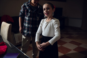 Young Girl Dancer Rehearses at Home with Family Nearby, Smiling and Preparing to Perform
