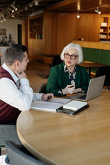 Senior woman mentor explaining business ideas to male colleague during focused mentoring session...
