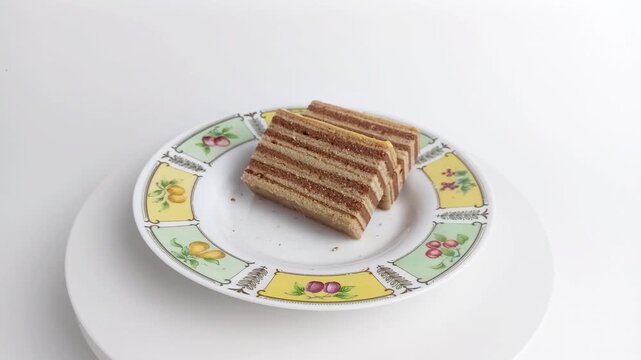 Hand picking up slice of lapis legit layer cake from plate. Traditional Indonesian spekkoek dessert. Sweet snack concept on white background.
