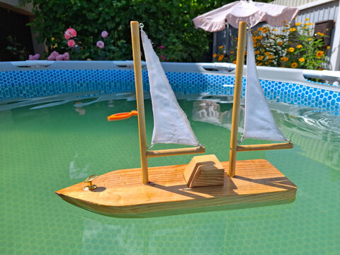 Wooden toy yacht with sails in outdoor man-made open-air swimming frame pool
