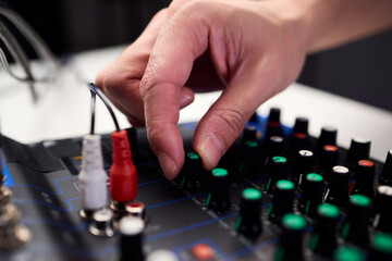 Fototapeta premium Closeup of hands adjusting mixer with glowing LED indicators and cables, Detailed image of operator controlling mixer dials and monitoring sound through sensors and LEDs