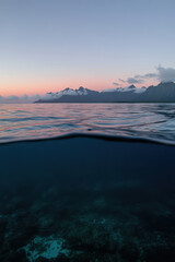 Calm water surface reflecting mountains under a twilight sky in a remote coastal area