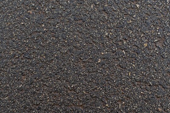 Dark, wet, and rough texture of asphalt or bituminous concrete, showing fine aggregate, perfect as a background for road or industrial surfaces.