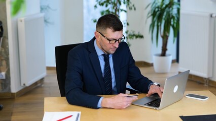 video. Caucasian businessman in black suit and blue shirt is sitting at the table, working on his...