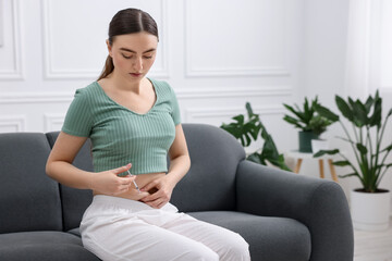 Obraz premium In vitro fertilisation. Woman making injection into her belly on sofa indoors, space for text