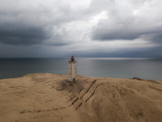 solitary lighthouse atop vast sand dunes, calm, expansive sea, dramatic, overcast skies. coastal landscape, isolation, resilience, and natural beauty, travel, navigation, moody seascapes.