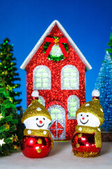 Two identical snowmen near a red Christmas house