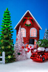 A snowman and a glass Christmas tree with a red car near a red Christmas house